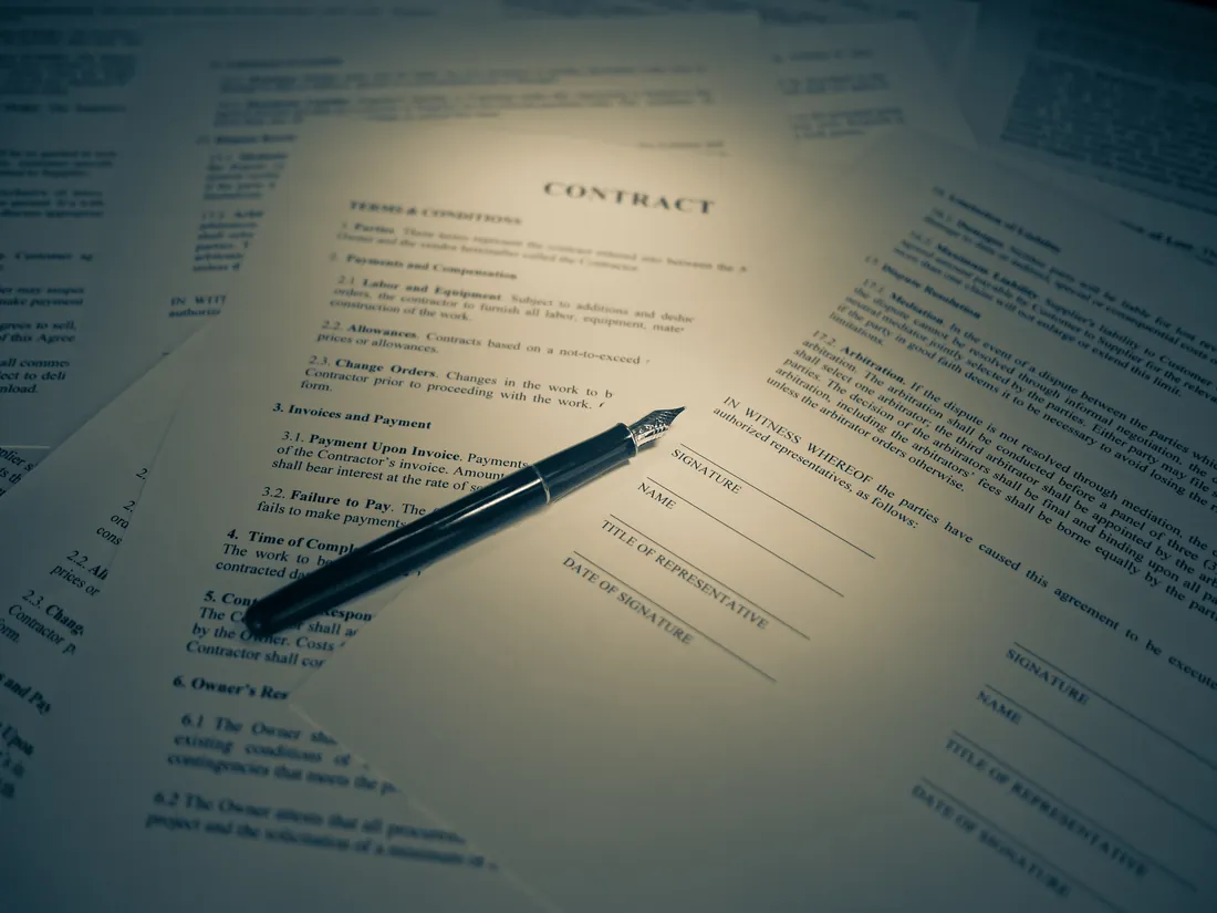 Avtaledokumenter med overskriften Contract spredt utover et bord, med en fyllepenn liggende ved signaturfeltene