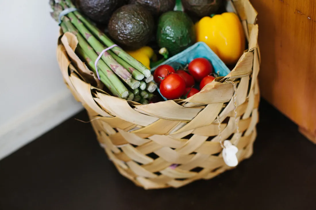 Flettet handlekurv med asparges, avokado, tomater og paprika, satt ned ved en trebenk